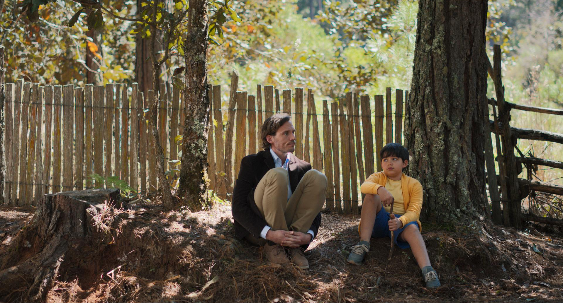 Man and a child in front of a fence, scene from a film. Photo/image: ‘The Book of Love’ courtesy of XYZ Films